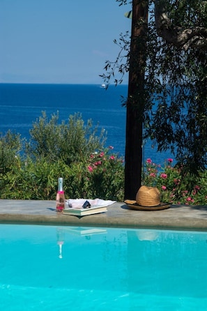 A poolside view with a clear blue sky, a bottle, a hat, and a book on a table. - Astryneon Suite, Divine Sea Views, Private Pool, Furnished Terrace, Paxos (Paxos)
