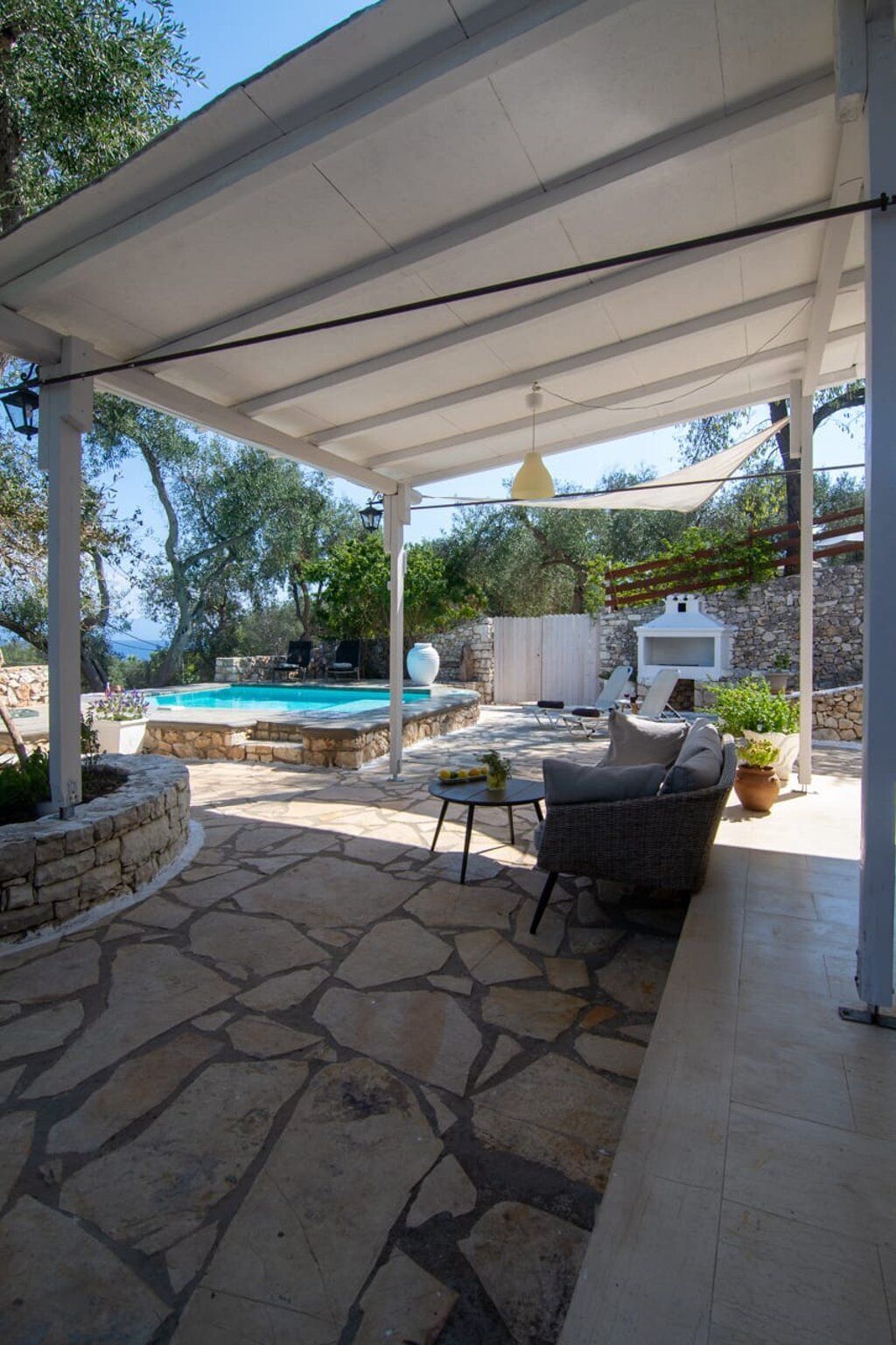 A covered patio with a stone floor, a pool, outdoor furniture, and a stone wall.