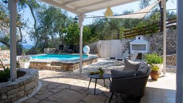 A covered patio with a stone floor, a pool, outdoor furniture, and a stone wall.