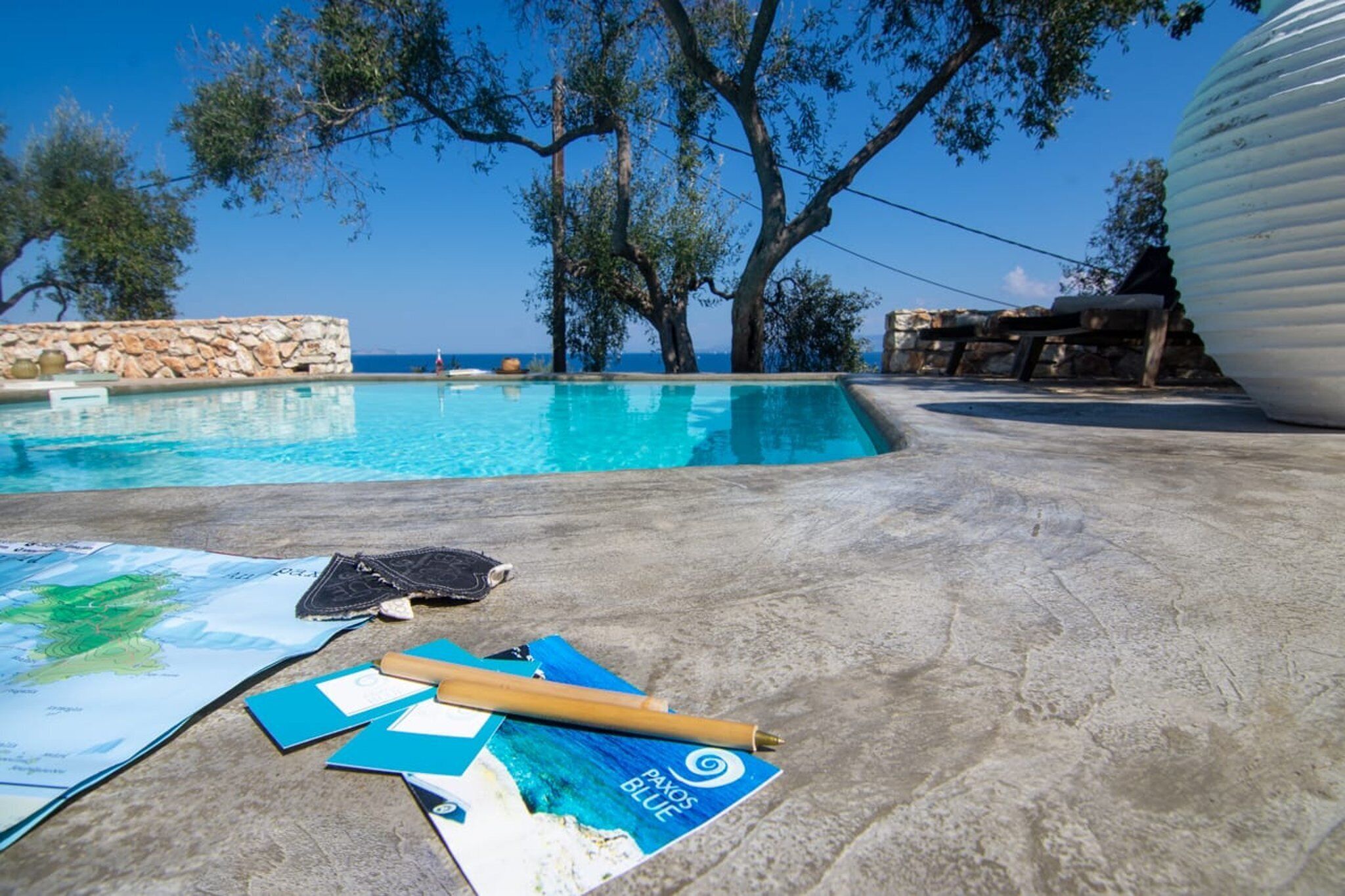Zona de piscina con pared de piedra, sillas de descanso y un mapa en el suelo.