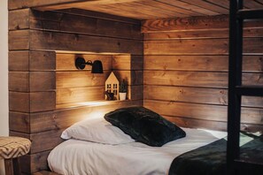 A wooden cabin-style room with a bed, pillows, a shelf with decorative items, and a ladder. - Moonshine Cabin (Big Bear Lake)