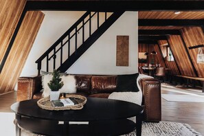 A loft-style room with a staircase, leather sofa, and a round coffee table. - Moonshine Cabin (Big Bear Lake)