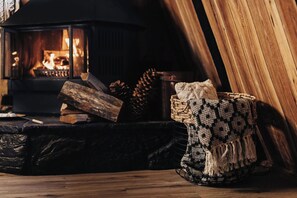 A cozy fireplace with logs, a woven basket, and a crocheted throw on a wooden floor. - Moonshine Cabin (Big Bear Lake)