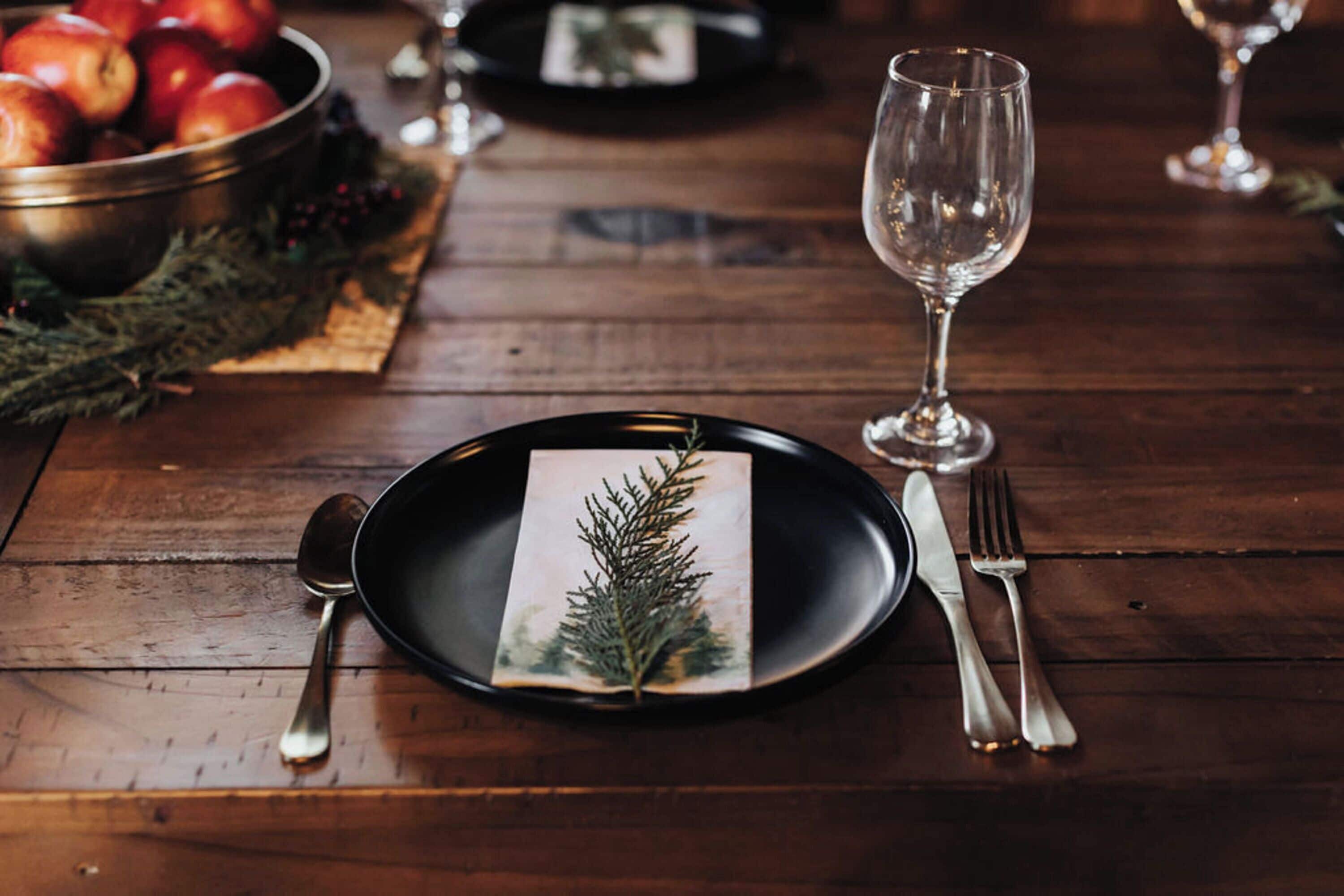 A wooden table with a black plate, a glass, a fork, and a spoon.