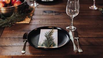 A wooden table with a black plate, a glass, a fork, and a spoon.