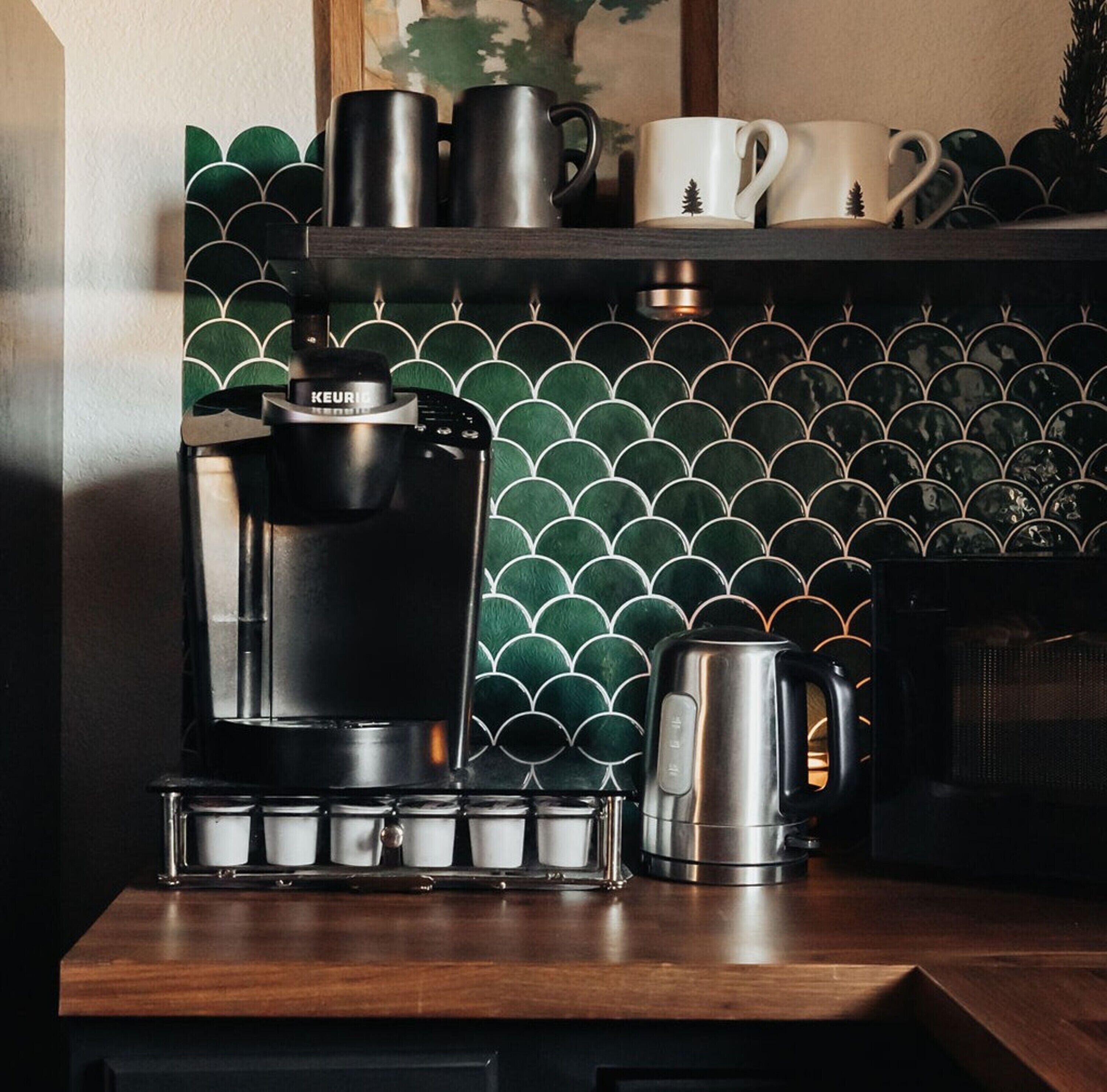 A coffee maker with a drip tray, a kettle, and a coffee mug on a wooden countertop.