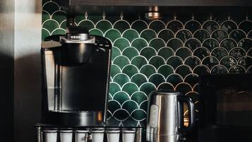 A coffee maker with a drip tray, a kettle, and a coffee mug on a wooden countertop.