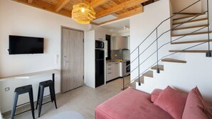 En moderne stue med træloft, et fladskærms-tv, en lyserød sofa og en trappe, der fører til et køkken.