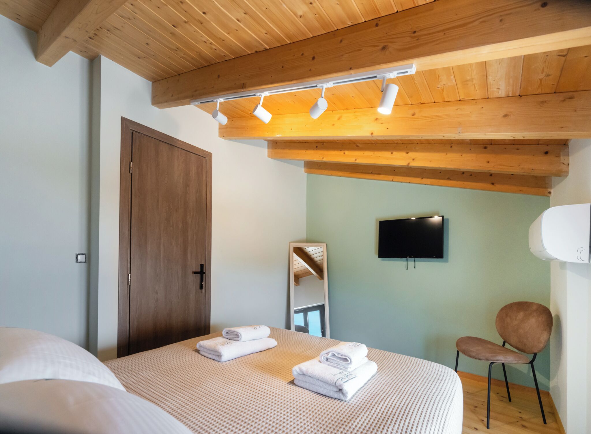 Une chambre avec un plafond en bois, un lit avec des serviettes, une chaise, une télévision et un miroir.
