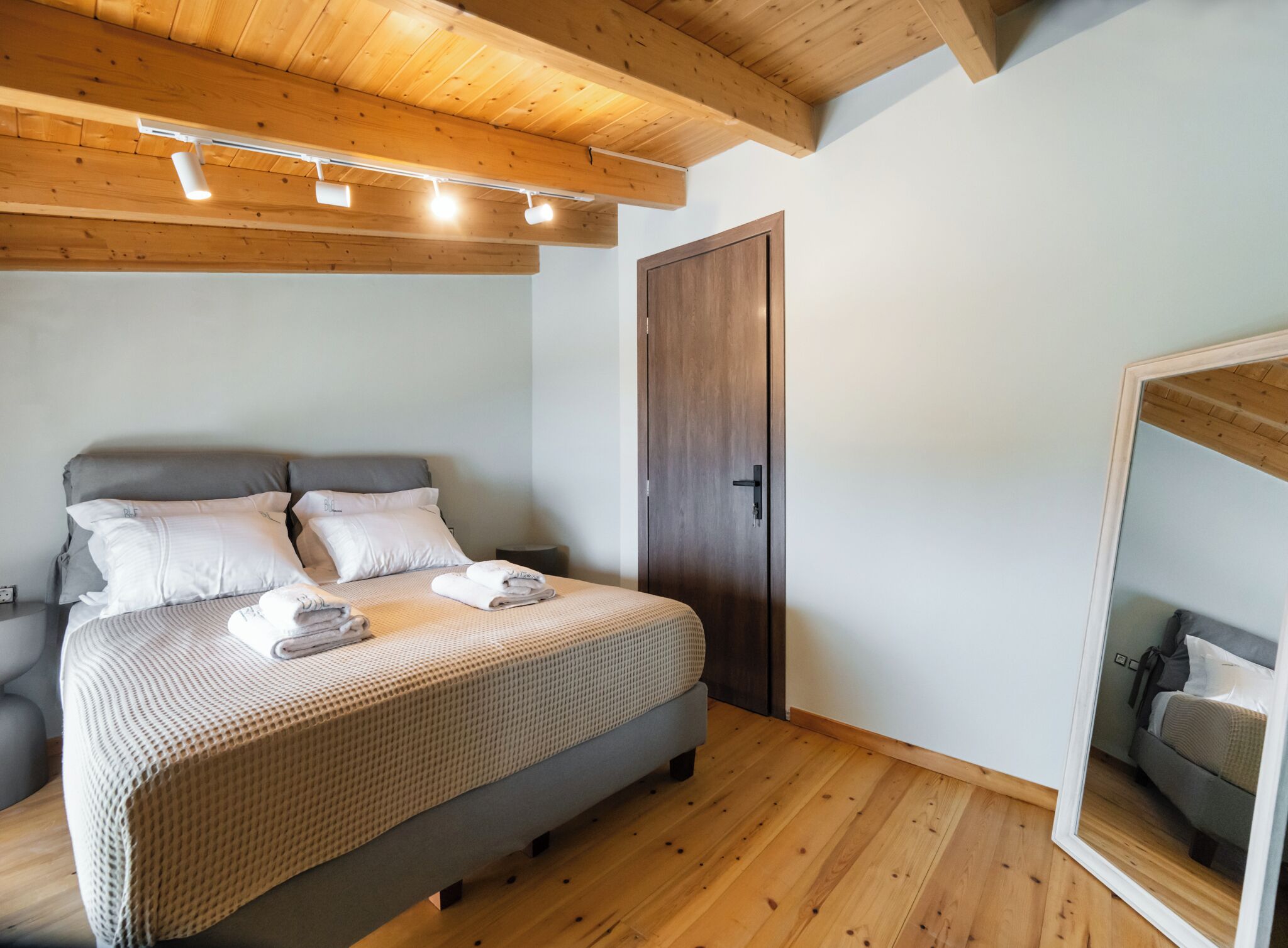 Ein Schlafzimmer mit einem Bett, Holzboden, einer Tür und einem Spiegel.
