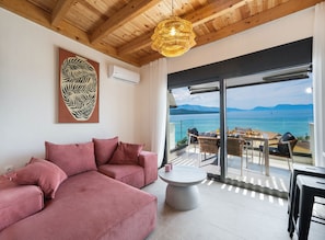 A modern living room with a sectional sofa, a round coffee table, and a view of the sea through large glass doors. - Blue Horizon (Lefkada)