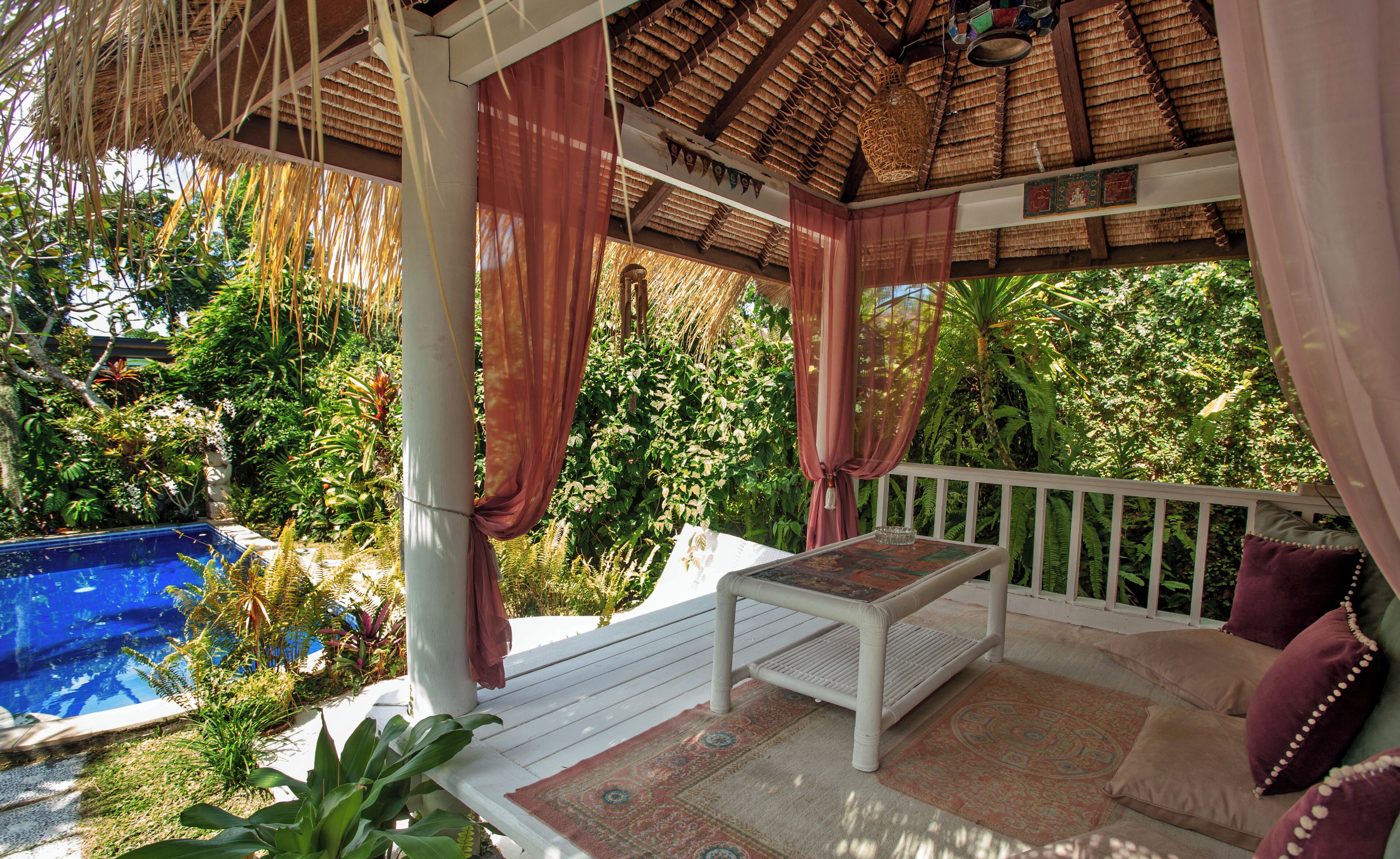 A covered outdoor area with a pool, a table, and a bench.