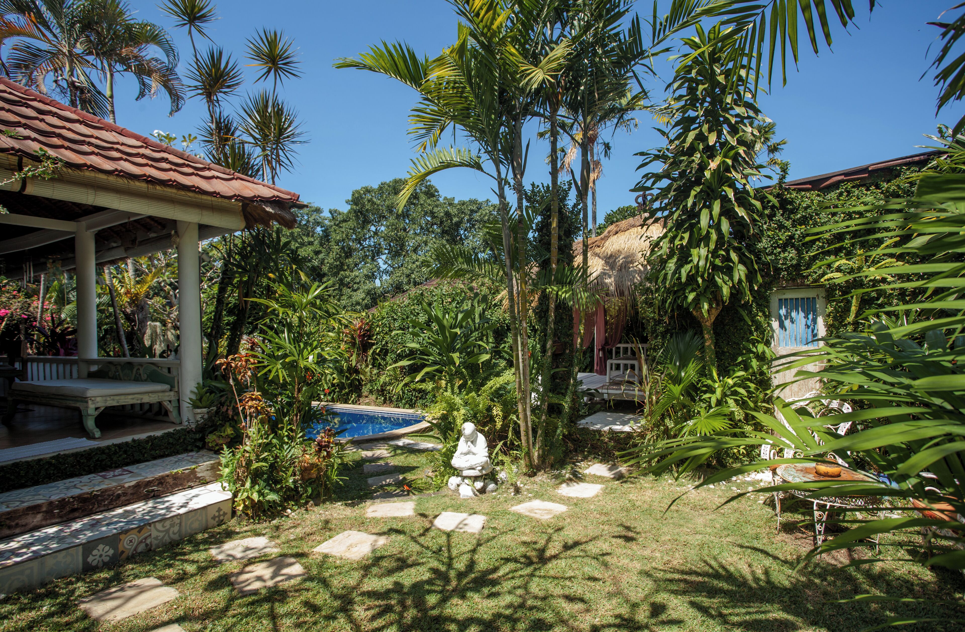 Un jardín con piscina, palmeras y un pabellón.