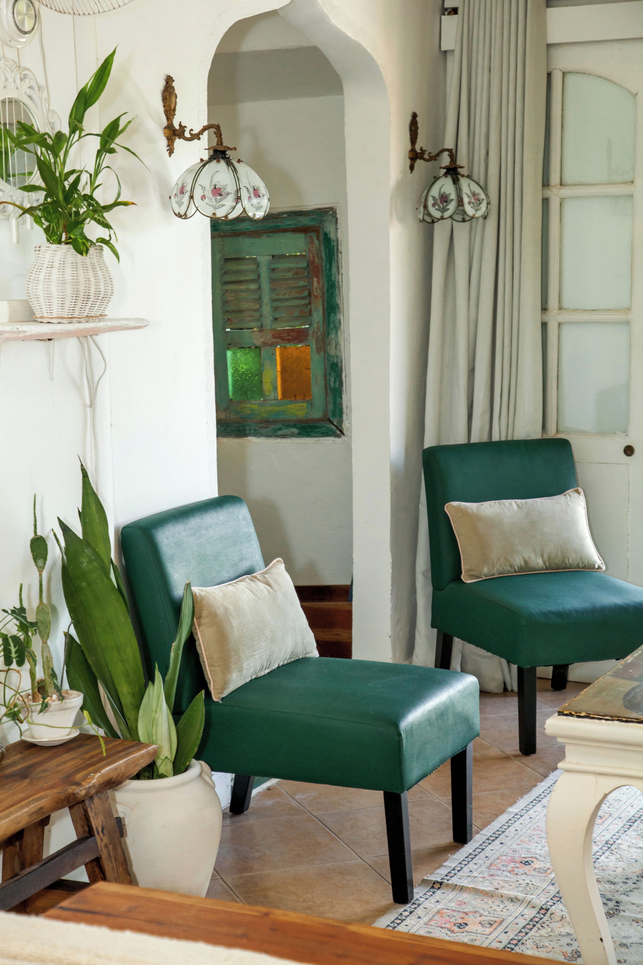 A room with two green armchairs, a white vase with a plant, a wooden table, and a patterned rug.