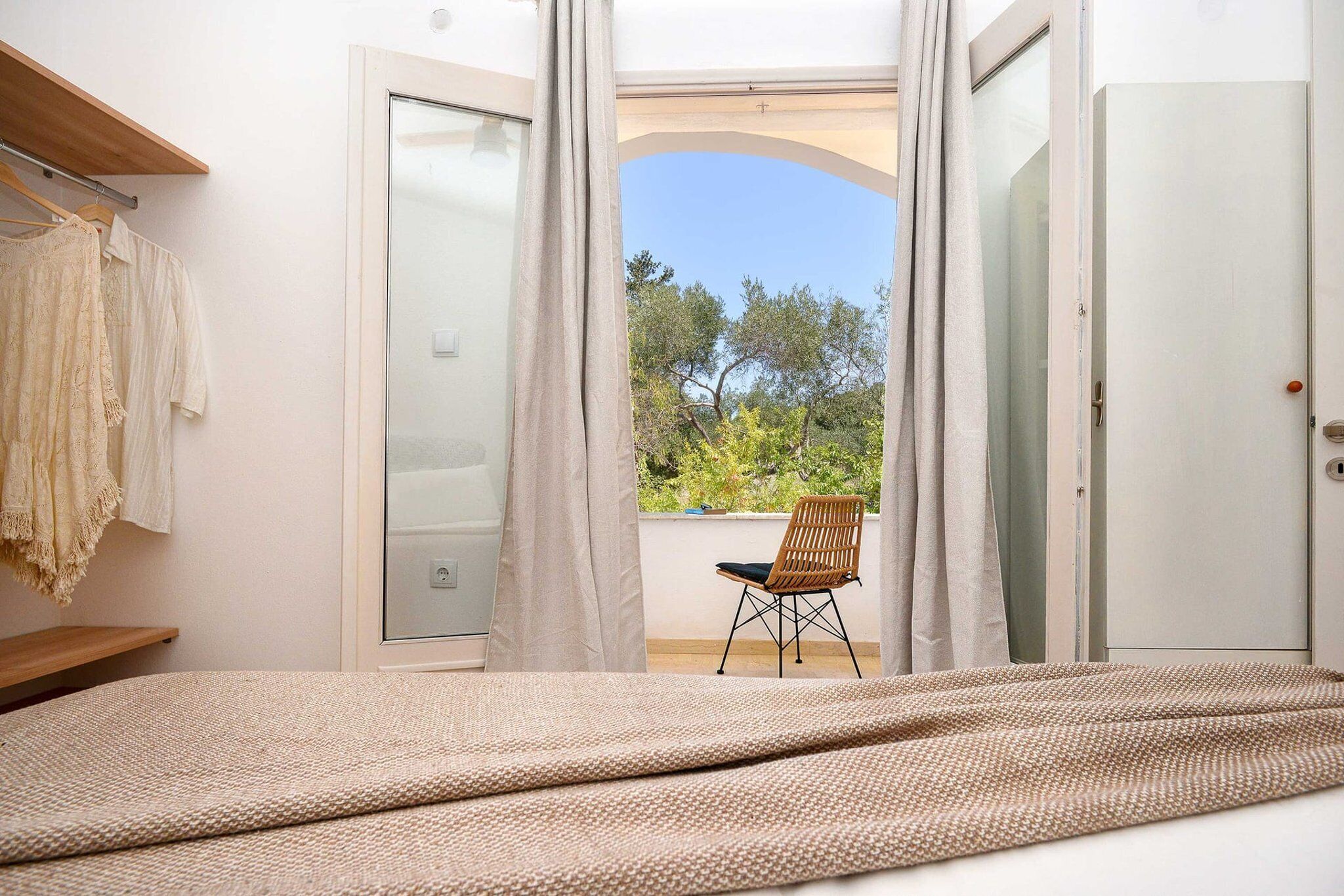 A bedroom with a bed, a chair, a wardrobe, and a window with curtains.
