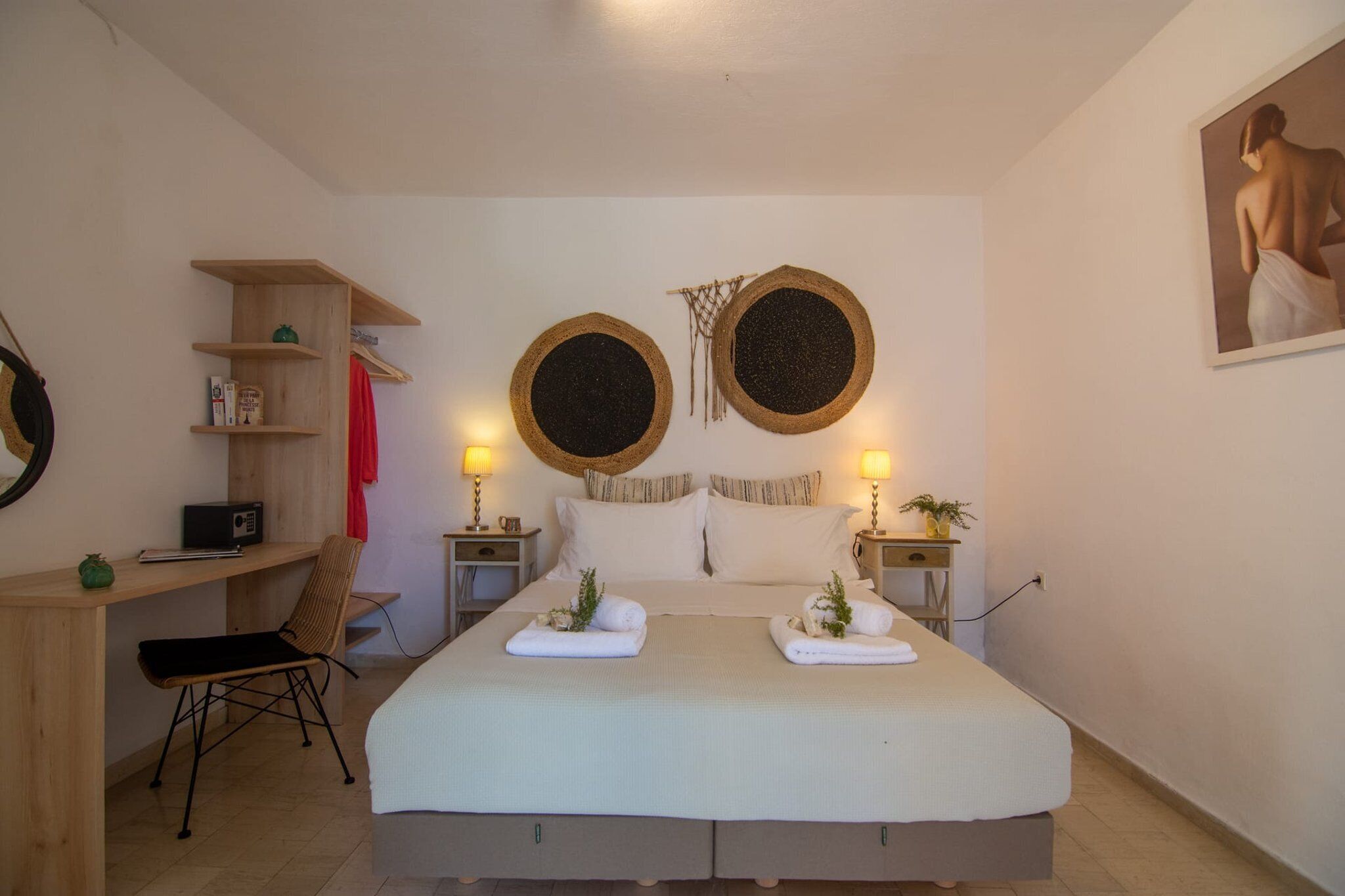 A bedroom with a bed, bedside tables, a desk, a chair, and a shelf with items.