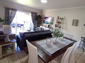 Ein Wohnzimmer mit Sofa, Fernseher, Esstisch und Stühlen.