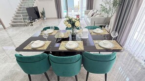 Un coin repas avec une table en bois foncé, dressée pour six personnes, des chaises en velours vert et un vase rempli de fleurs.