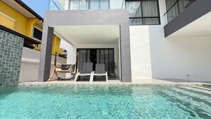 Une piscine avec des chaises longues, un hamac et l’entrée du bâtiment.