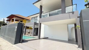 Ein modernes, zweistöckiges Haus mit Swimmingpool, geschlossenem Eingangsbereich und einem Balkon.