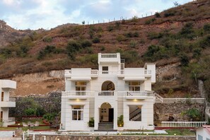Un edificio de varios pisos con entrada central, balcones y un muro de contención de piedra.