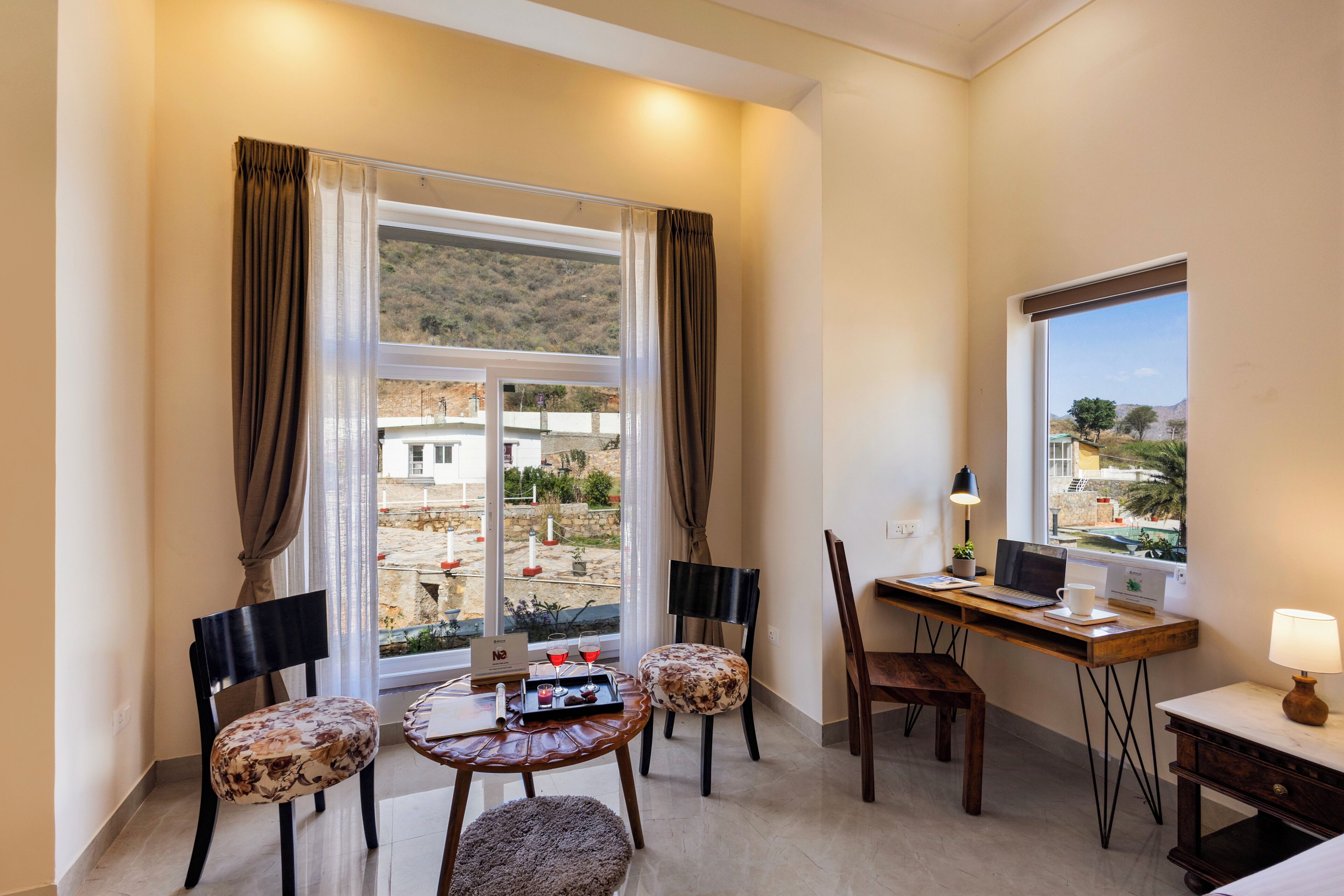A room with a desk, chairs, a laptop, a lamp, and a view of a courtyard.
