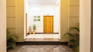 Un couloir avec une porte en bois, des plantes en pot et des tableaux encadrés accrochés au mur.