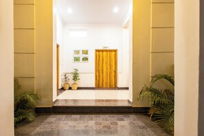 Un pasillo con puerta de madera, plantas en macetas e imágenes enmarcadas en la pared.
