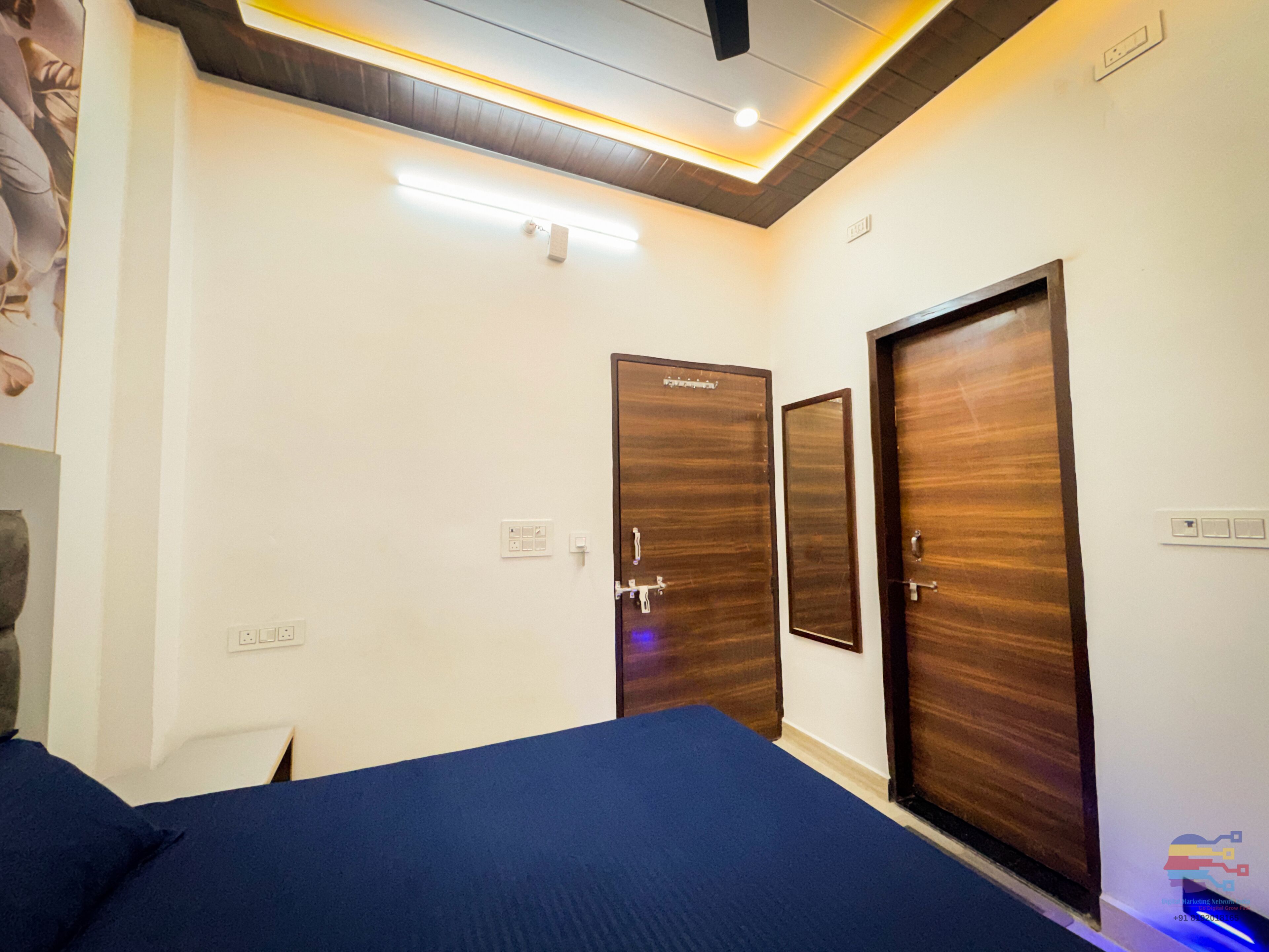 A hotel room with a bed, two wooden doors, a blue carpet, and a ceiling light fixture.