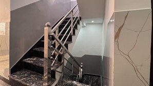 Una escalera moderna con escalones de mármol y barandillas metálicas, que conduce a un rellano con un muro de cristal.