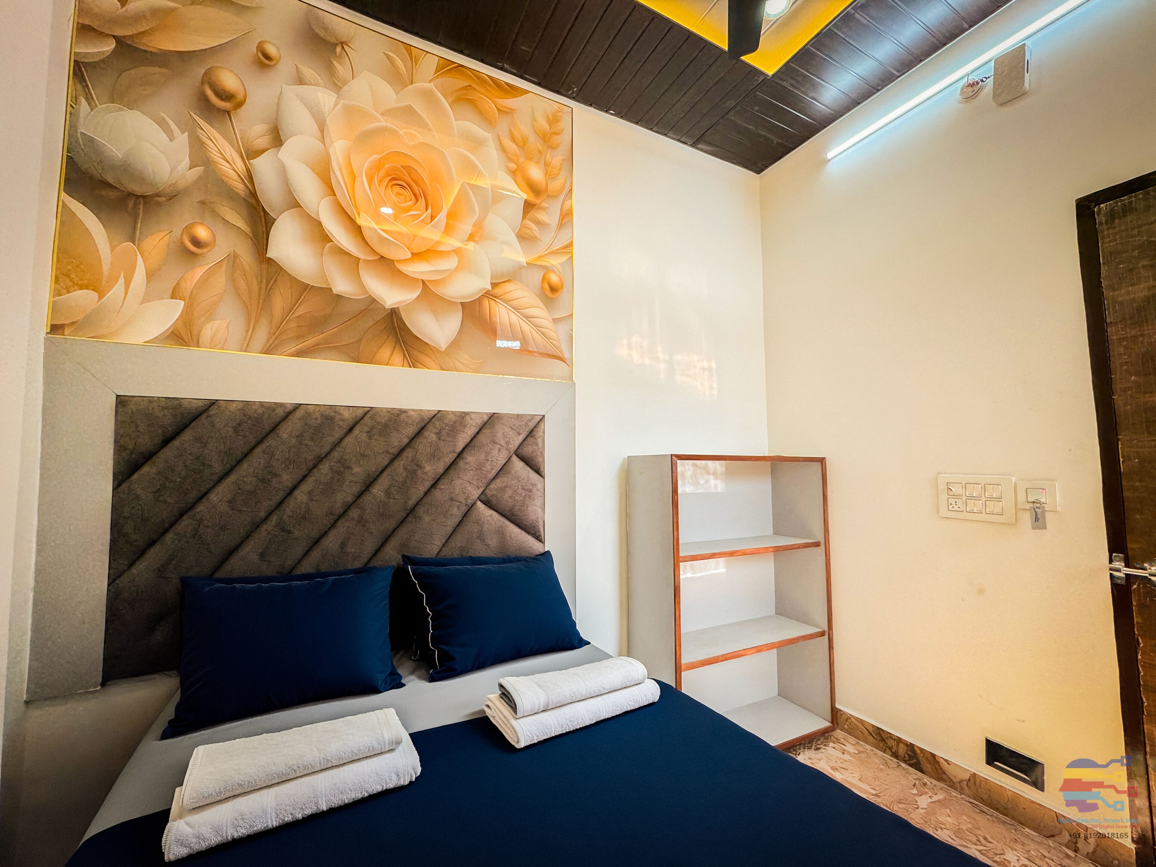 A bedroom with a bed, pillows, a headboard, a wall with a floral mural, a shelf, and a door.