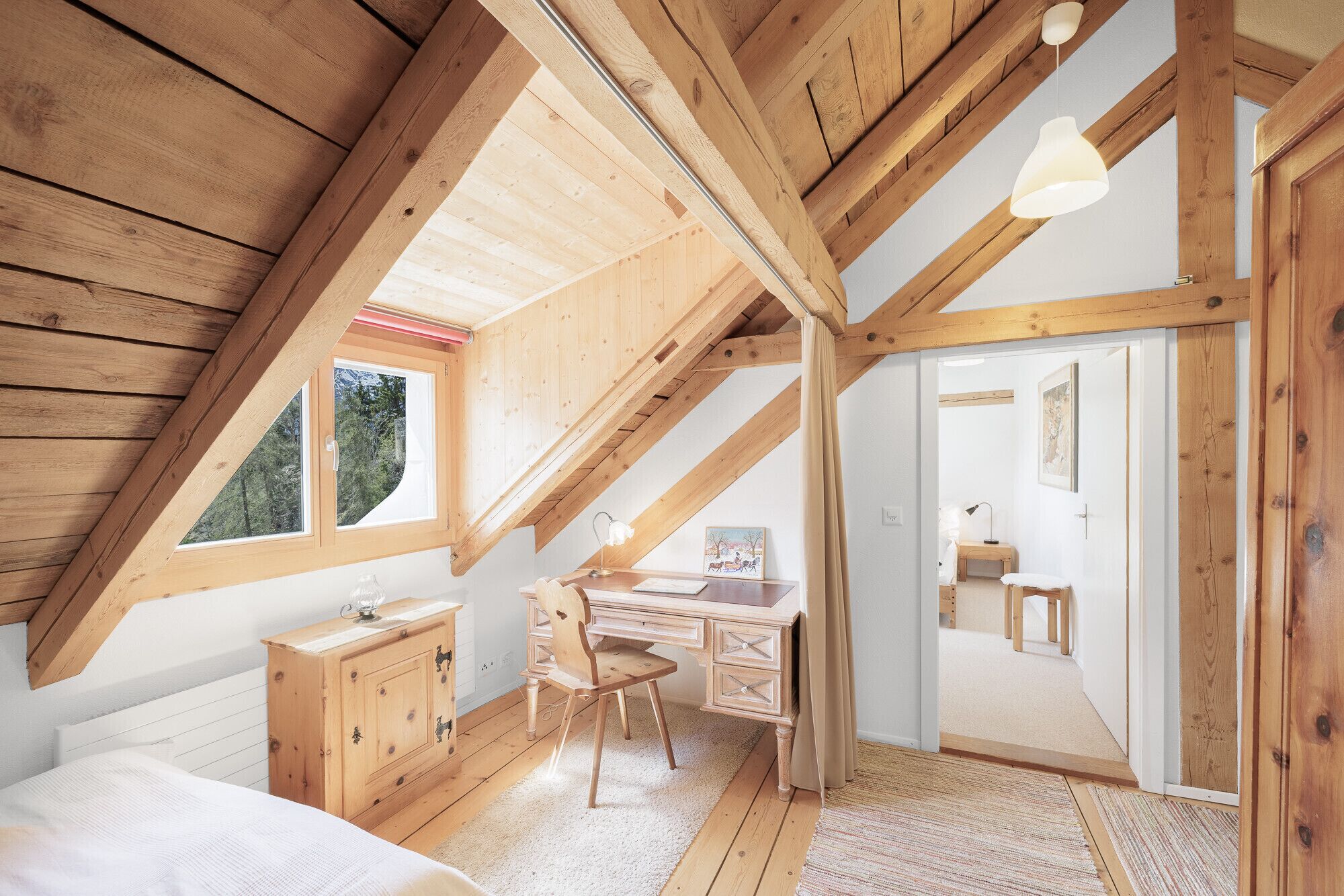 Une chambre avec un plafond en pente, des poutres en bois, un bureau, une chaise et un lit.