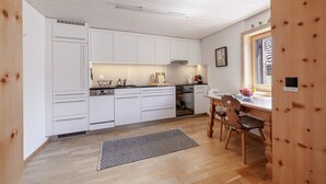 Une cuisine moderne avec des meubles blancs, un lave-vaisselle, un four et un coin repas comprenant une table et des chaises.