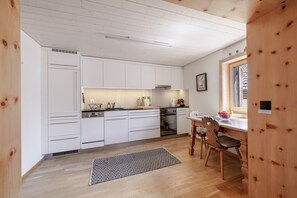 Eine moderne Küche mit weißen Schränken, einem Geschirrspüler, einem Backofen und einem Essbereich mit Tisch und Stühlen.