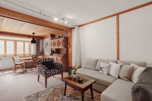 Ein gemütliches Wohnzimmer mit einer Couch, einem gemusterten Sessel, einem Holztisch und einem Teppich.