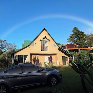 Una casa de dos pisos con techo verde, un coche estacionado en la entrada y un cielo azul despejado.