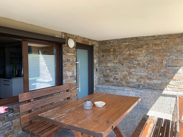 An outdoor patio with a wooden table, benches, and a stone wall.