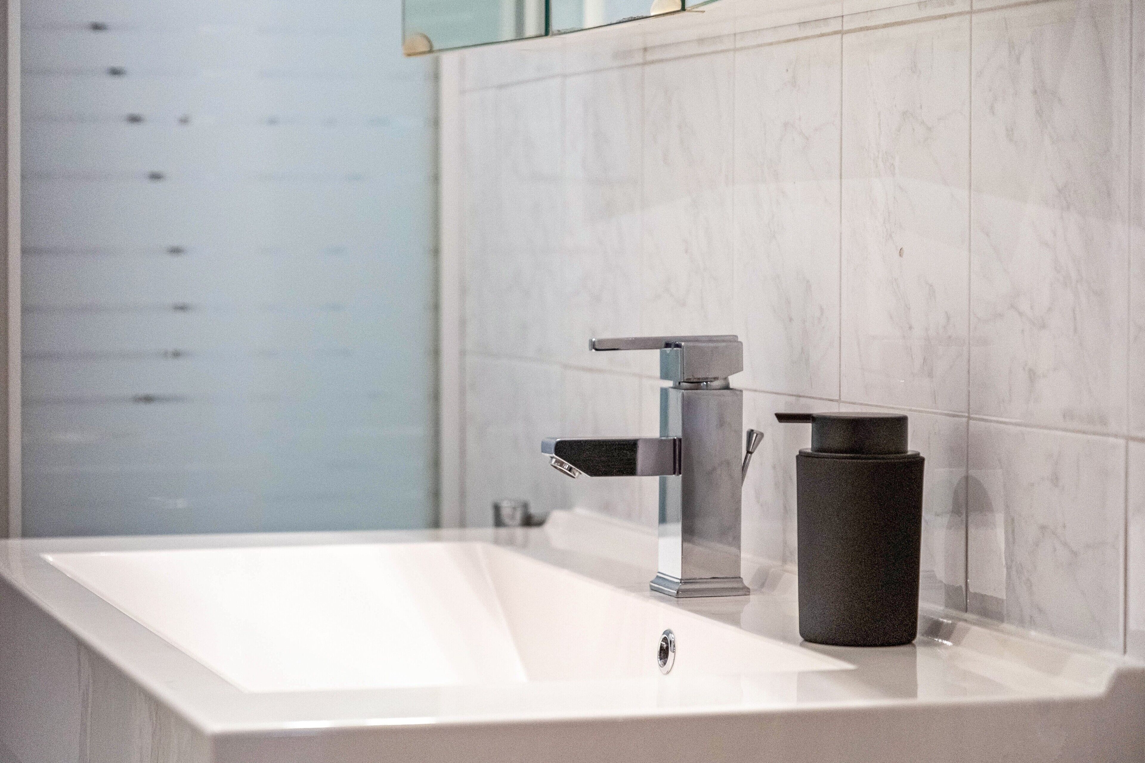 A modern bathroom with a rectangular sink, a single faucet, and a black soap dispenser.
