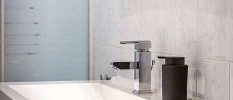A modern bathroom with a rectangular sink, a single faucet, and a black soap dispenser.