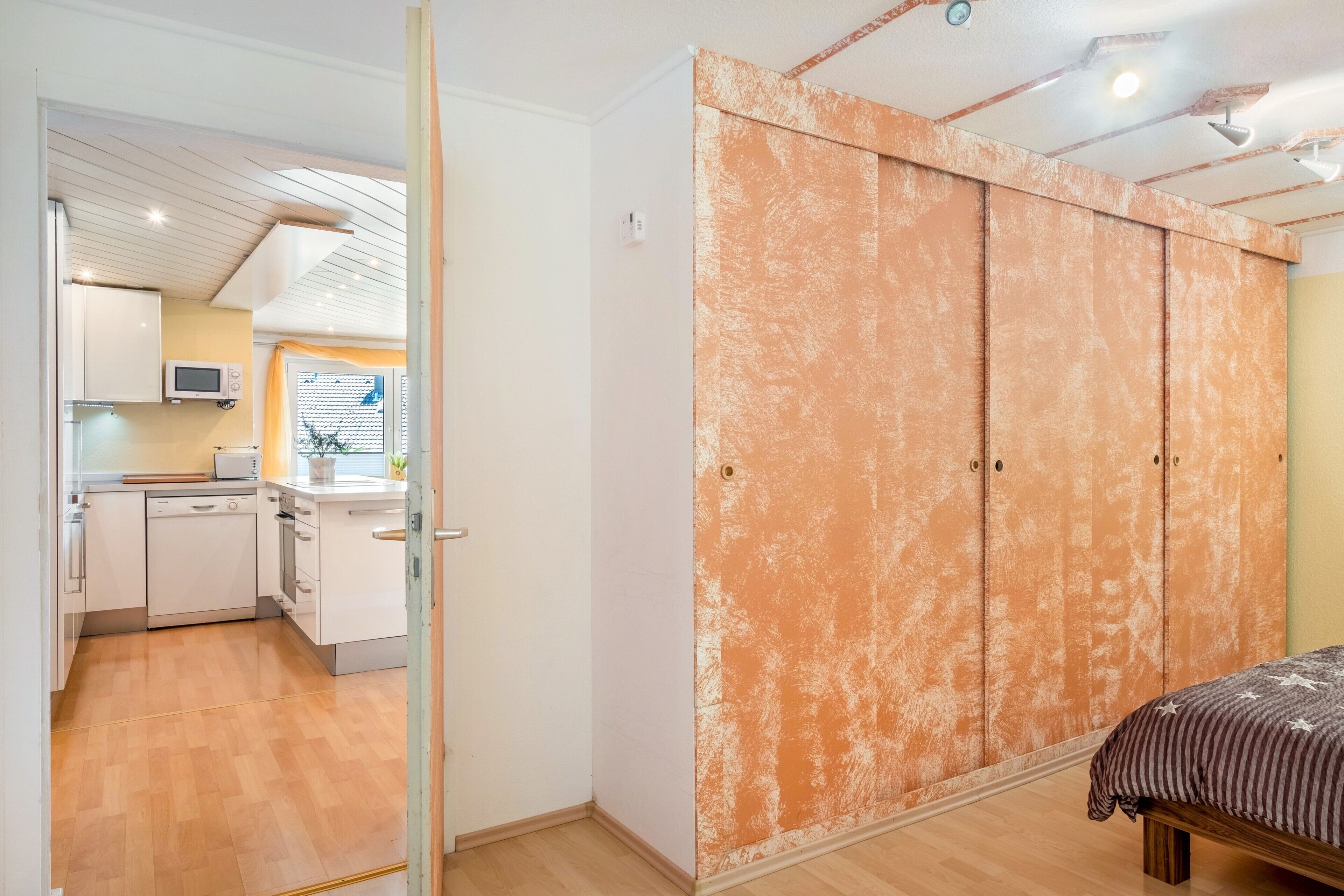 A bedroom with a bed, a wardrobe, and a kitchenette in the adjacent room.