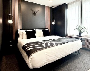 Ein modernes Hotelzimmer mit einem großen Bett, einem aufgehängten Hirschgeweih an der Wand und einem Fenster mit Vorhängen.