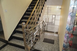 Una escala amb barana metàl·lica i un aplom, que condueix a una habitació amb cortina estampada.