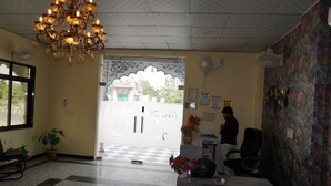 A reception area with a chandelier, a checkered floor, a potted plant, a desk, and a wall with framed certificates. - Moon Mahal Hotel (Amer)