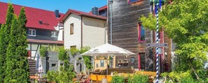 Ein BIERGARTEN mit Außenbestuhlung, einem Holzzaun und einem Gebäude mit rotem Dach.