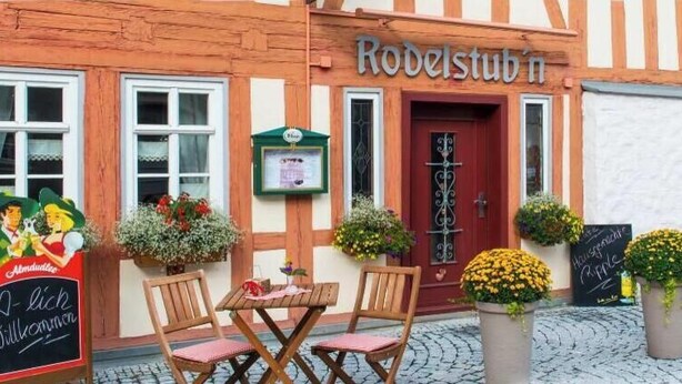 A traditional building with a sign 'Rodelstüb'n' and outdoor seating with tables and chairs.