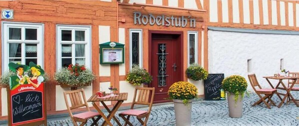 Ein traditionelles Gebäude mit einem Schild 'Rodelstüb'n' und Außenbereich mit Tischen und Stühlen.
