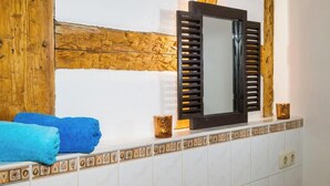 A bathroom with a wooden beam, a mirror with shutters, blue towels, and decorative tiles.
