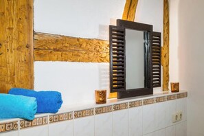 Ein Badezimmer mit Holzbalken, einem Spiegel mit Rollläden, blauen Handtüchern und dekorativen Fliesen.