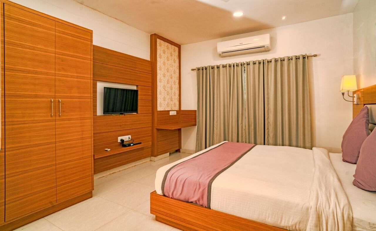 A bedroom with a bed, wardrobe, TV, air conditioning unit, curtains, and a lamp.