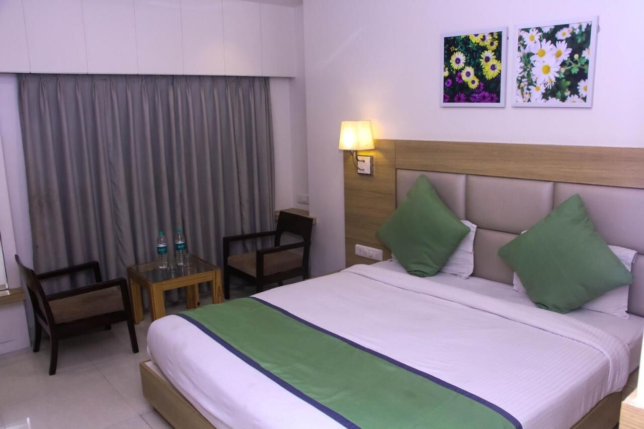 A hotel room with a bed, a chair, a small table with bottles, and two wall-mounted lamps.